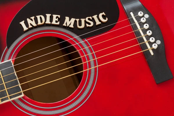 Words Indie Music with wooden letters, closeup on a surface of red acoustic guitar. Music entertainment background.