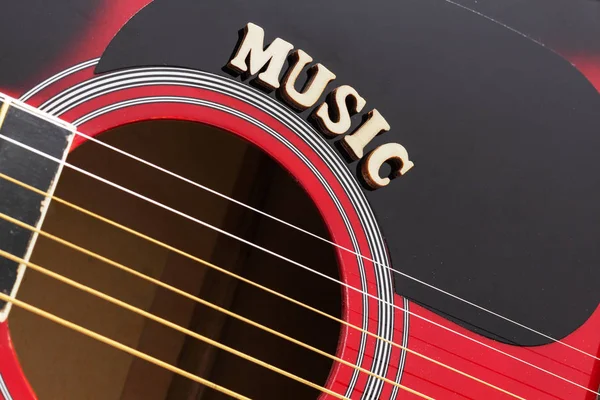 Word Music with wooden letters, closeup on a surface of red acoustic guitar. Music entertainment background.