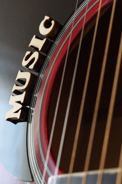 Word Música con letras de madera, primer plano sobre una superficie de guitarra acústica roja. Fondo de entretenimiento musical . — Foto de Stock