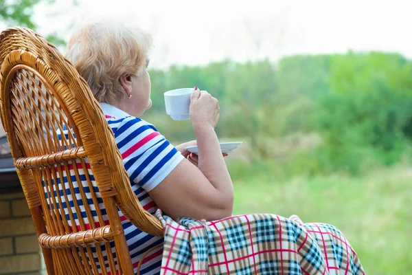 Starsza Kobieta Siedzi Fotelu Biegunach Wiklinowe Pije Kubek Gorącej Herbaty — Zdjęcie stockowe