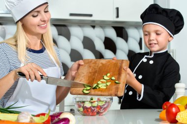 Bir aşçı ailesi. Sağlıklı beslenme. Anne ve çocuklar mutfakta sebze salatası hazırlıyor..