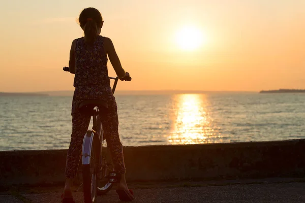 The girl on the bike looks at the sunset.