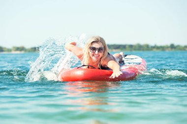 Kürek tahtasında yüzen genç seksi kadın. Su sporları, aktif yaşam tarzı..