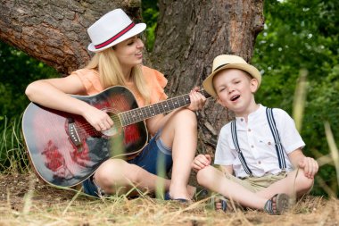 Genç anne ve güzel bir oğlan dinlenme ormandaki şarkı şarkıları bir gitar altında.