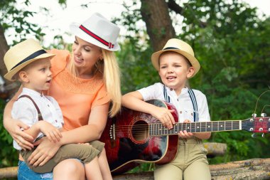 Genç anne ve iki oğlu ormanda, Zihnimin içinde şarkılar bir gitar ile dinlenme.
