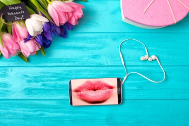 Buket laleler ve bir hediye kutusu ile Sevgililer günü arka plan. İleti bir öpücükle. Hareket eden telefon ve kulaklık kalp şeklinde.