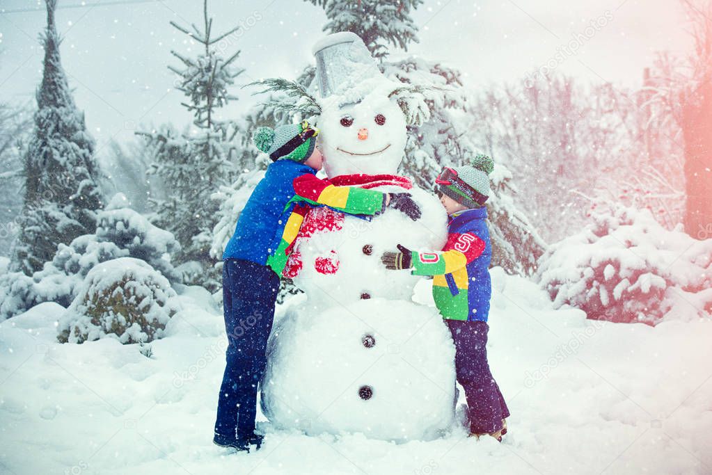 Children in a winter snowy forest mold a big snowman.Family winter fun for Christmas vacation.
