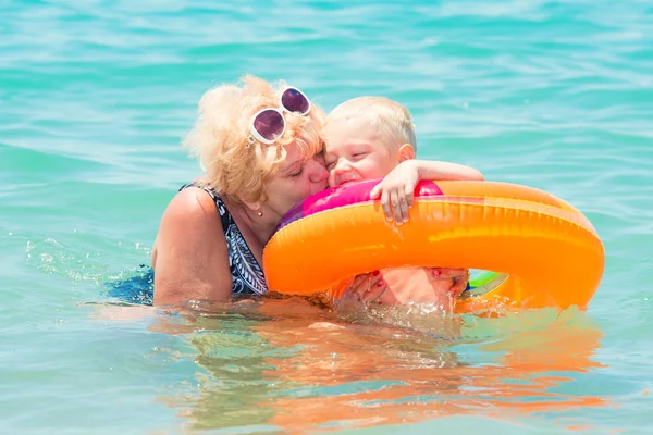 Grandmother and little grandson swim in the sea.The baby in the bouncy multicolored circle.Summer vacation.