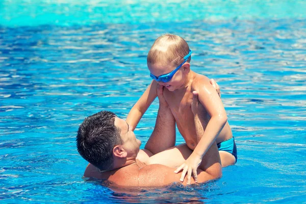Father and son jump and swim in the pool under sun light at summer day. Leisure and swimming at holidays.