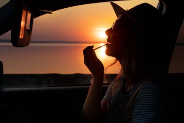 Güzel bir kadın arabada dudaklarını boyar. Akşam günbatımında gezinti güvertesinde.