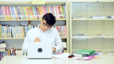 Kütüphane genç öğrenci çalışmada zor. Asyalı erkek üniversite öğrenci kitaplığı kitap ve Resepsiyon ve gülümseyen laptop ile çalışma araştırma yapıyor. Okul eğitim teknoloji kavramı için geri.