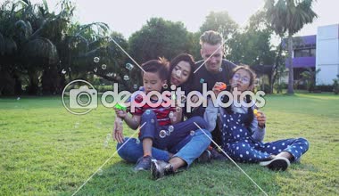 Aile parkta kabarcık üfleme. Beyaz adam, Çinli kadın ve çocukları ile karışık yarış ailesi. Park içinde çim birlikte eğlenmek birlikte oturmak.