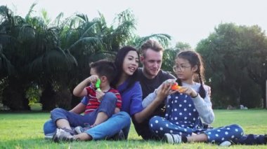 Aile parkta kabarcık üfleme. Beyaz adam, Çinli kadın ve çocukları ile karışık yarış ailesi. Park içinde çim birlikte eğlenmek birlikte oturmak.