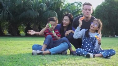 Aile parkta kabarcık üfleme. Beyaz adam, Çinli kadın ve çocukları ile karışık yarış ailesi. Park içinde çim birlikte eğlenmek birlikte oturmak.
