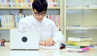 Kütüphane genç öğrenci çalışmada zor. Asyalı erkek üniversite öğrenci kitaplığı kitap ve Resepsiyon ve gülümseyen laptop ile çalışma araştırma yapıyor. Okul eğitim teknoloji kavramı için geri.