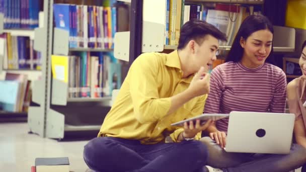 亚洲大学生活理念 有吸引力的亚洲女学生在图书馆做研究 她的男学生朋友在笔记本和笔记本电脑上注意到 以书架为背景 — 图库视频影像