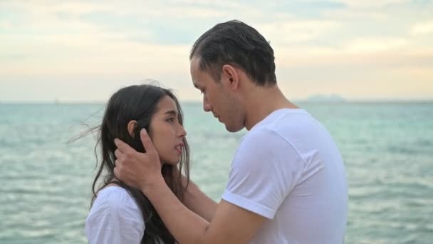 ビーチで魅力的な若いカップルのロマンス 太陽の中に一緒に情熱的なキスを設定します 代前半の白人男性で若い中国の女性 スローモーションで撮影します 映画を見る — ストック動画