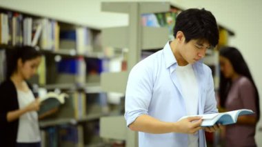 Kütüphanede kitap okuyan genç bir erkek öğrenci.