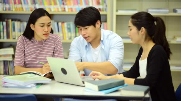 若い学生は 図書館で勉強します 机の上の本を図書館で研究をやって幸せのアジア女性と男性大学生研究ノート 学校教育多様性概念に戻るのため — ストック動画
