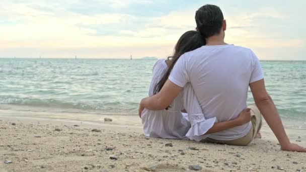 魅力的な若いカップルがビーチで楽しんで 座って海を見ています 代前半の白人男性で若い中国の女性 — ストック動画