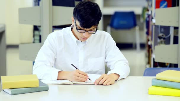 年轻的学生在图书馆努力学习 亚洲男大学生在图书馆做学习研究在书桌和微笑的书 回归学校教育多元化理念 — 图库视频影像