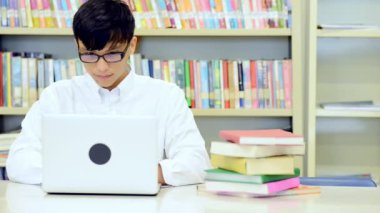 Kütüphane genç öğrenci çalışmada zor. Asyalı erkek üniversite öğrenci kitaplığı kitap ve Resepsiyon ve gülümseyen laptop ile çalışma araştırma yapıyor. Okul eğitim teknoloji kavramı için geri.