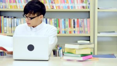 Kütüphane genç öğrenci çalışmada zor. Asyalı erkek üniversite öğrenci kitaplığı kitap ve Resepsiyon ve gülümseyen laptop ile çalışma araştırma yapıyor. Okul eğitim teknoloji kavramı için geri.