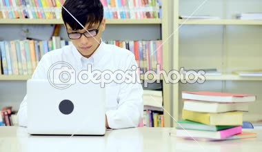 Kütüphane genç öğrenci çalışmada zor. Asyalı erkek üniversite öğrenci kitaplığı kitap ve Resepsiyon ve gülümseyen laptop ile çalışma araştırma yapıyor. Okul eğitim teknoloji kavramı için geri.