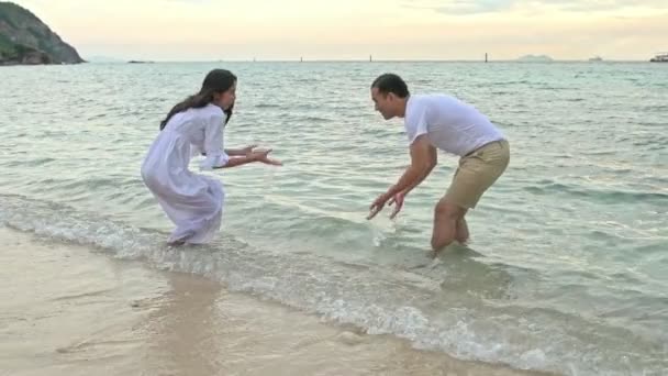 魅力的な若いカップルがビーチで楽しんで 水しぶき 代前半の白人男性で若い中国の女性 スローモーションで撮影します 映画を見る — ストック動画