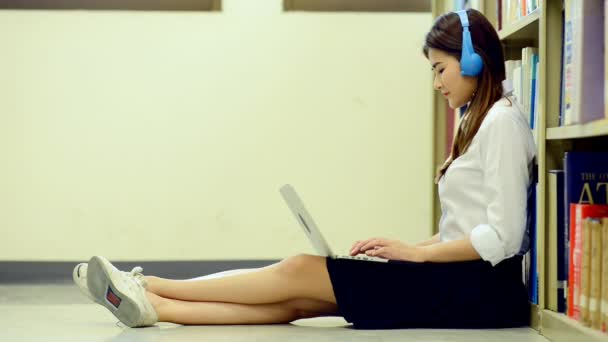 年轻的学生在图书馆努力学习 亚洲女大学生在图书馆做研究在地板上的笔记本电脑和听音乐 回归学校教育技术理念 — 图库视频影像
