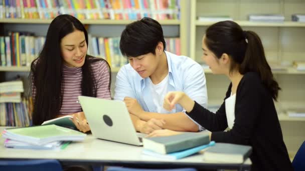 若い学生は 図書館で勉強します 机の上の本を図書館で研究をやって幸せのアジア女性と男性大学生研究ノート 学校教育多様性概念に戻るのため — ストック動画