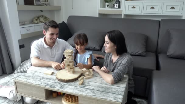 小女孩和爸爸妈妈在起居室里玩游戏 美丽的白色孩子玩块与她的母亲和她英俊的美国丈夫在家里下午 — 图库视频影像