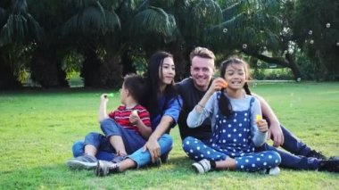 Aile parkta kabarcık üfleme. Beyaz adam, Çinli kadın ve çocukları ile karışık yarış ailesi. Park içinde çim birlikte eğlenmek birlikte oturmak.
