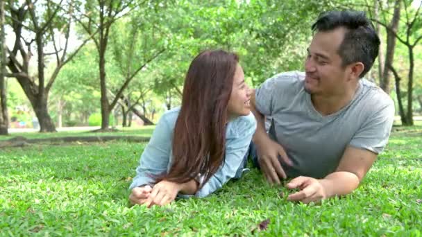 公園でリラックス甘いカップル 草の上に敷設される若いアジア人男性と女性が一緒にリラックスして 公園でロマンチックなアクションを行います — ストック動画