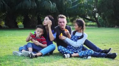 Aile parkta kabarcık üfleme. Beyaz adam, Çinli kadın ve çocukları ile karışık yarış ailesi. Park içinde çim birlikte eğlenmek birlikte oturmak.