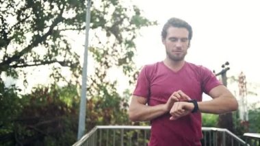 Runner spor akıllı saatine bakıyor. Onun fitness performansını gerçek zamanlı kontrol etmek için. Beyaz kırmızı gömlekli erkek.