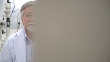 Gözlükçü, iş portre. Üst düzey Çinli gözlükçü göz görme ölçüm makinesi yanındaki oturma portre. Gerçek gözlükçü hastane odasında. Tıp kavramı.