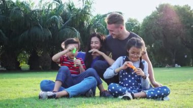 Aile parkta kabarcık üfleme. Beyaz adam, Çinli kadın ve çocukları ile karışık yarış ailesi. Park içinde çim birlikte eğlenmek birlikte oturmak.