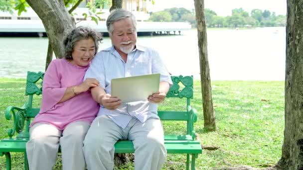 Pareja Mayor Parque Mirando Cuaderno Hablando Entre Divirtiéndose Sentado Banco — Vídeo de stock