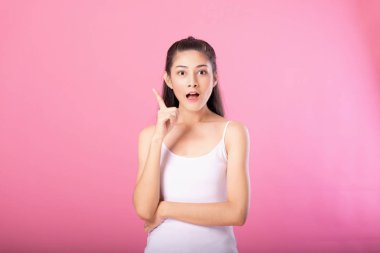 Beyaz tanktop kıyafeti süre ayakta ve pembe arka plan üzerinde izole kamera gülümseyen düşünme poz ile gülümseyen bir çekici kadın portresi.