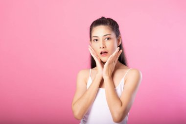 Beyaz tanktop kıyafeti süre ayakta ve pembe arka plan üzerinde izole kamera gülümseyen sürpriz poz ile gülümseyen bir çekici kadın portresi.