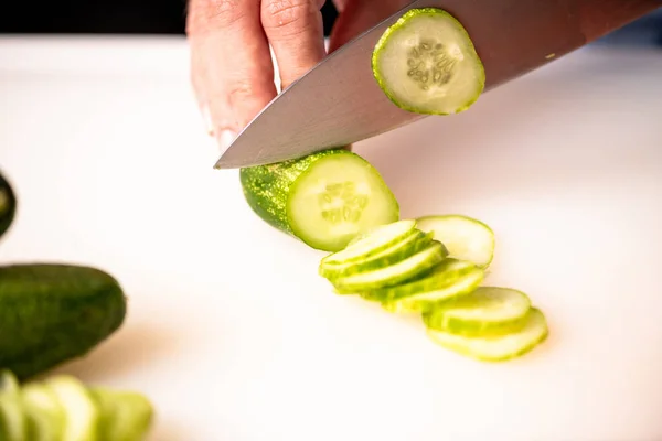 Woman chopping cucumber in kitchen.