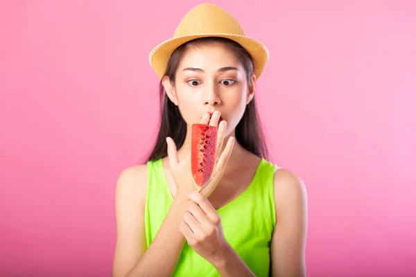 Portrait of a happy attractive woman in summer green outfit with hat holding fresh water melon on stick looking surprise isolated over pink background. Summer vibe concept.