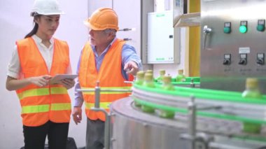 Senior kalite müfettişi fabrika genç takım üyesi öğretim. Çin eski erkek genç ekibiyle şişe üretim hattında arka plan ile kalite sorunu tartışıyor.