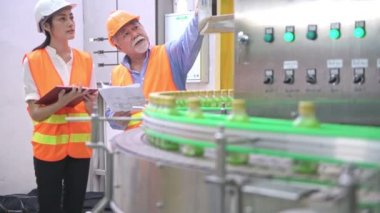 Senior kalite müfettişi fabrika genç takım üyesi öğretim. Çin eski erkek genç ekibiyle şişe üretim hattında arka plan ile kalite sorunu tartışıyor.