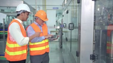 Senior kalite müfettişi fabrika genç takım üyesi öğretim. Çin eski erkek genç ekibiyle şişe üretim hattında arka plan ile kalite sorunu tartışıyor.