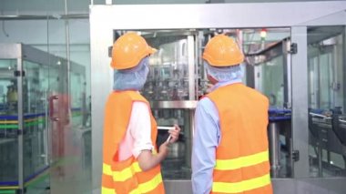 Senior kalite müfettişi fabrika genç takım üyesi öğretim. Çin eski erkek genç ekibiyle şişe üretim hattında arka plan ile kalite sorunu tartışıyor.