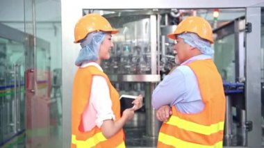 Senior kalite müfettişi fabrika genç takım üyesi öğretim. Çin eski erkek genç ekibiyle şişe üretim hattında arka plan ile kalite sorunu tartışıyor.
