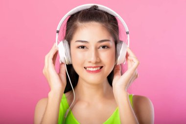 Pembe arka plan üzerinde izole onun kulaklık ile müzik yaz kıyafeti mutlu bir çekici kadın portresi.