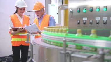 Senior kalite müfettişi fabrika genç takım üyesi öğretim. Çin eski erkek genç ekibiyle şişe üretim hattında arka plan ile kalite sorunu tartışıyor.